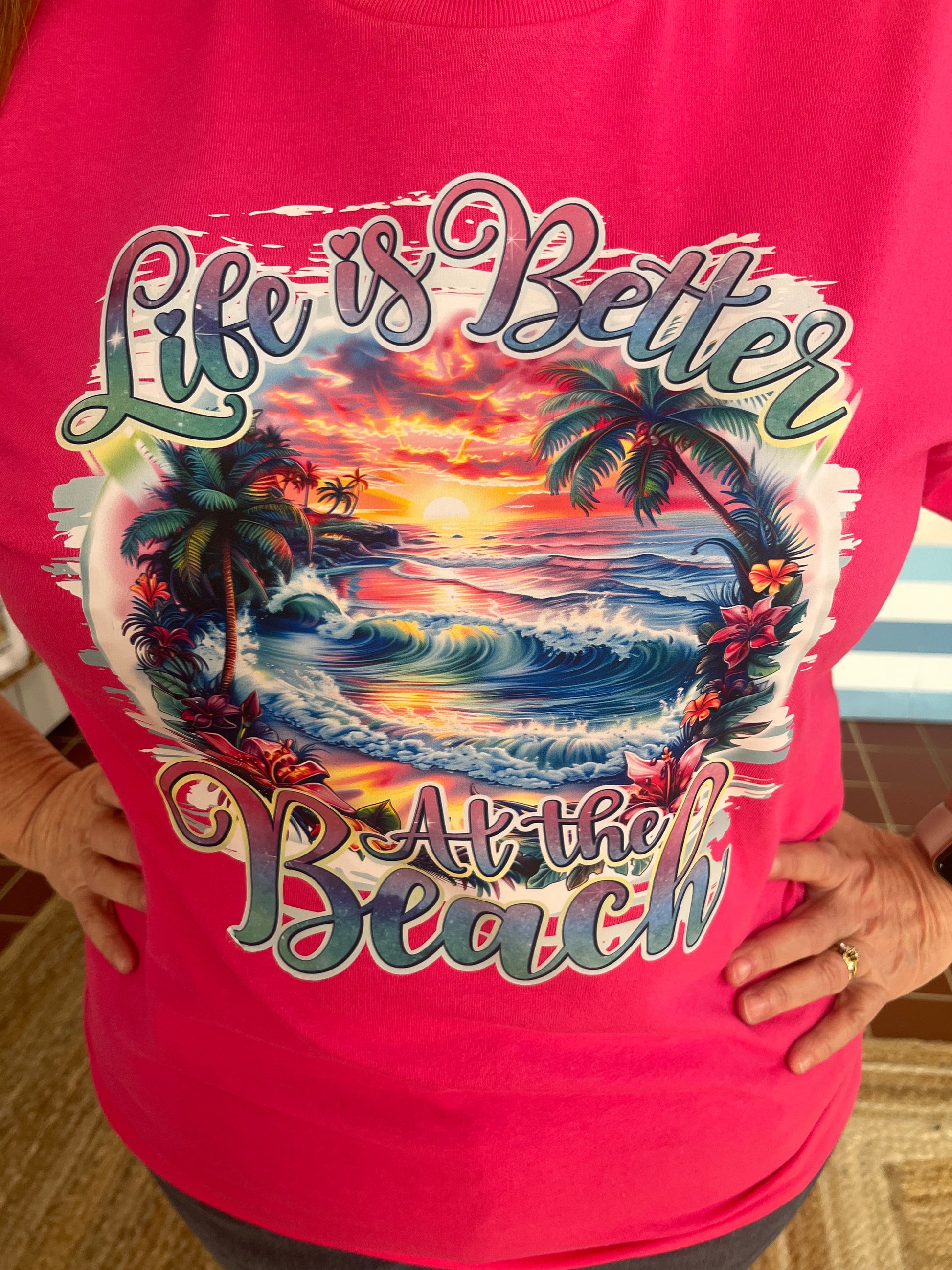 Life is Better Graphic T, available in sizes Small though XL in Hot Pink or Jade.  Graphic T Features a beautiful, vibrant sunset on the beach, with palm trees.