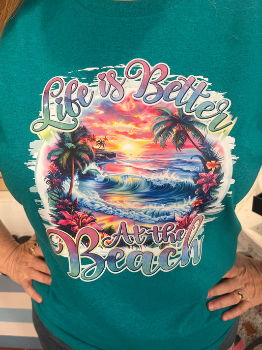 Life is Better Graphic T, available in sizes Small through XL in Jade or Hot Pink.  This short sleeve graphic T displays a beautiful, vibrant sunset on the beach, with palm trees.